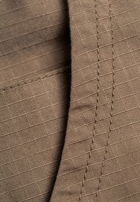 Nahaufnahme eines braunen Stoffs mit sichtbaren Nähten und einem gitterartigen gewebten Muster auf der Textiloberfläche.