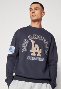 Sweatshirt bleu marine avec le texte et le logo "Los Angeles Dodgers", doté d'un col rond et de poignets côtelés. Texte imprimé en beige et bleu.