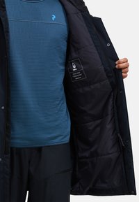 Mariene geïsoleerde jas met een rits aan de voorkant, voorzien van een blauw binnenlaag met een ruitpatroon en een merklabel aan de binnenkant.