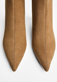 Tan suede nilkka-kengät teräväkärkisillä saumoilla, sileällä pinnalla ja hoikalla siluetilla, suunniteltu tiukaksi istuvuudeksi nilkan ympärille.