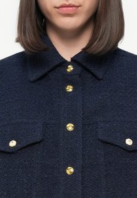 Navy blue textured shirt made of boucle fabric, featuring a pointed collar, chest pockets, and gold star-shaped buttons.