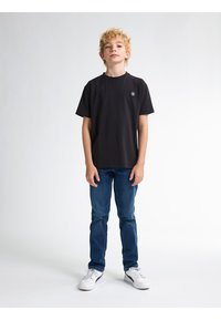 Černé bavlněné tričko s kulatým výstřihem a malou nášivkou loga na hrudi, spárované s modrými džíny a bílými teniskami.