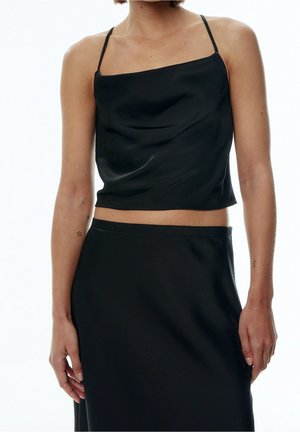 Femme portant un top court en satin noir avec fines bretelles et une jupe noire assortie, montrée des épaules aux hanches.