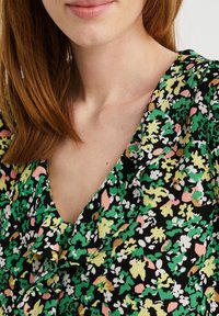 Black floral blouse featuring green, pink, and white patterns. It has a V-neckline with ruffled edges and a lightweight fabric texture.