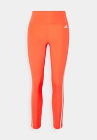 Leggings de sport taille haute orange vif avec des bandes blanches sur les côtés et un petit logo Adidas blanc sur la hanche gauche.