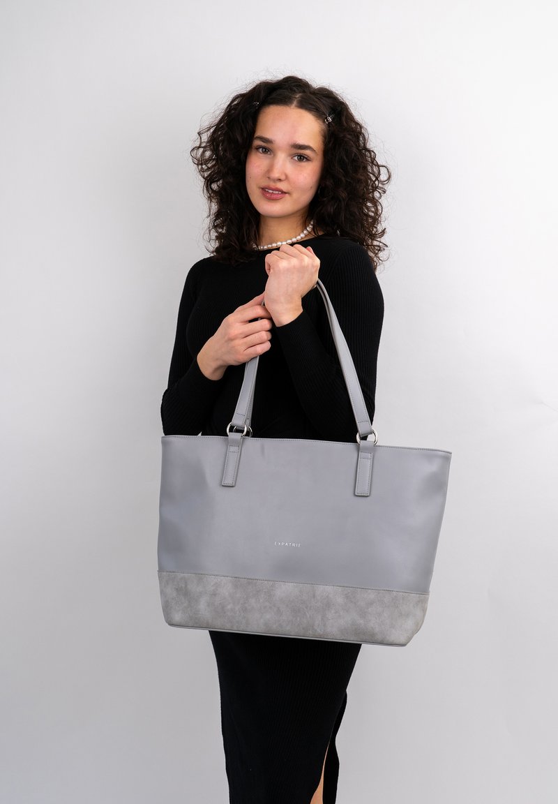 Gray tote bag with a smooth top section and textured gray bottom. Features sturdy straps and a subtle brand logo on the front.