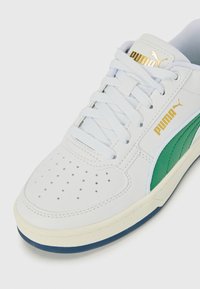 Witte leren sneakers met een groene accent, voorzien van perforaties op de teen, platte veters en een gouden logo. Getextureerde rubberen zool.