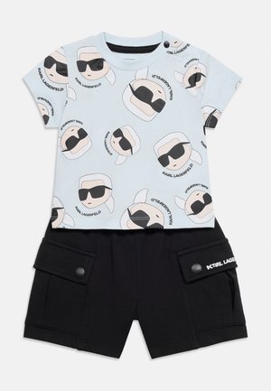 Peuterkleding met lichtblauw shirt met korte mouwen met tekenfilmgezichten met zonnebrillen en zwarte shorts met zijklepzakken.