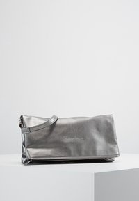 Hopeanvärinen metallinen iltalaukku, jossa on sileä pinta, pehmeä suorakulmainen muoto ja irrotettava kahva. Edessä kohopainettu brändäys.