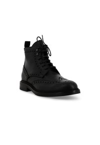 Stivaletti alla caviglia in pelle nera con dettagli brogue, punta rotonda, design con lacci e suola intermedia testurizzata a contrasto. Include una linguetta posteriore per facilitare la calzata.