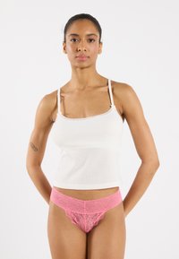 Witte geribde tanktop met delicate kantafwerking, gecombineerd met een roze kanten slipje met een golvende tailleband en ingewikkelde patronen.