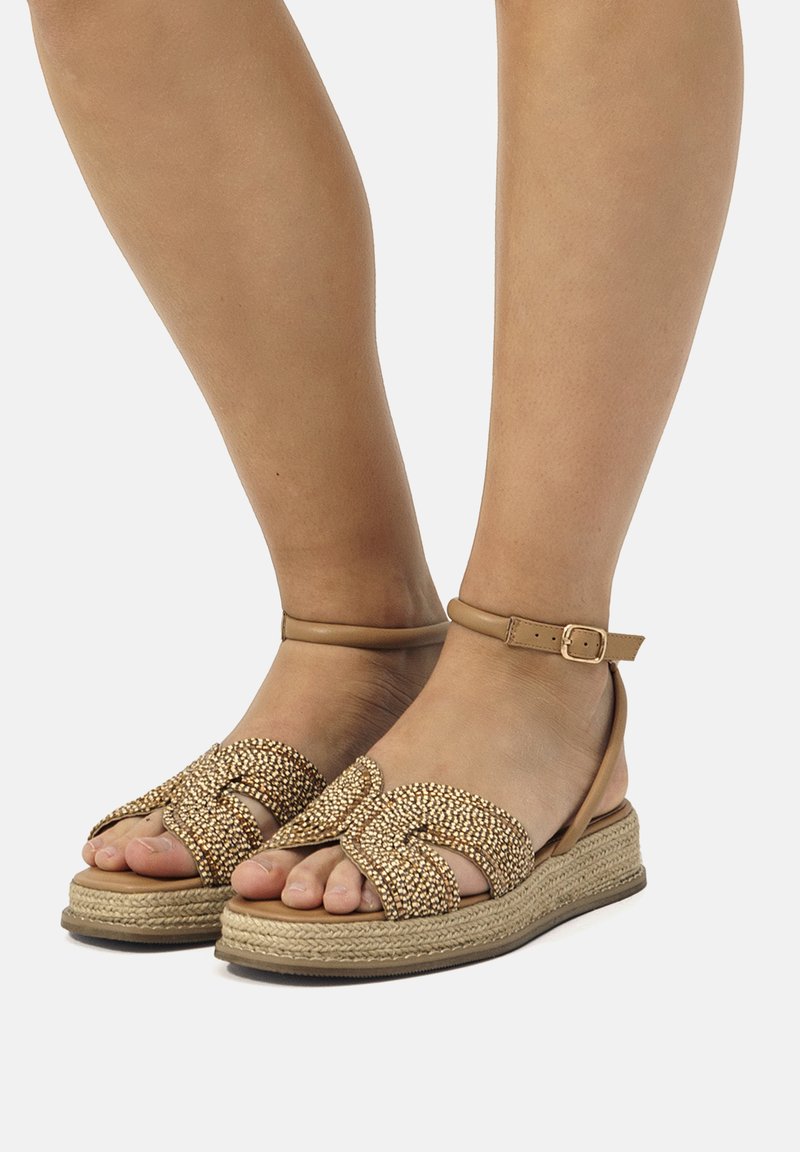 Sandales espadrilles tressées brunes avec un design entrecroisé et une sangle à la cheville, présentant une surface texturée et une semelle compensée en jute.