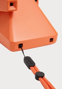Orange plastic product with a matte finish, featuring a textured grip and a black corded attachment with a branded tag.