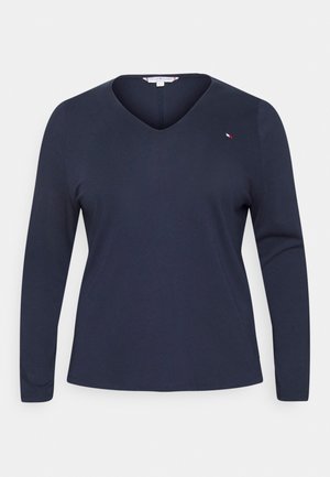 Marineblaues, langärmeliges V-Ausschnitt-Shirt mit einem kleinen gestickten Logo auf der linken Brust, vor einem einfarbigen Hintergrund gezeigt.