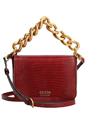 Czerwona torebka Guess ze strukturalnej skóry z masywnym, złotym łańcuchem jako uchem i regulowanym paskiem na ramię, logo oraz napis "EST 1981" złotymi literami.