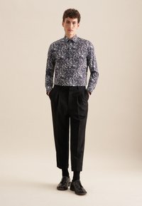 Camicia a maniche lunghe in navy con motivo paisley, abbinata a pantaloni neri plissettati e scarpe nere. Gli articoli presentano una vestibilità sartoriale e una texture liscia.