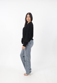 Maglione nero peloso, vestibilità comoda, con maniche lunghe. Indossato con jeans a vita alta blu chiaro e sandali con tacco a blocco trasparente.