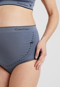 Sous-vêtements gris à côtes avec une bordure en dentelle noire et des coutures décoratives, portant le nom de marque "Cache Cœur" imprimé en noir.