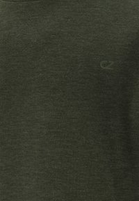 Chemise à manches courtes vert foncé avec une texture douce, présentant un logo discret dans la même teinte sur le devant. Encolure lisse et côtelée.