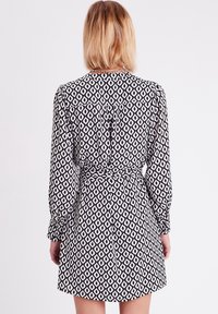 Robe à motifs noir et blanc, à manches longues, taille ceinturée et corsage ajusté s'évasant en une jupe courte.