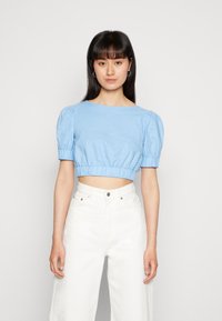 Top cropped azul claro com mangas bufantes e gola redonda, com bainha franzida, combinado com calças brancas de perna larga de cintura alta.