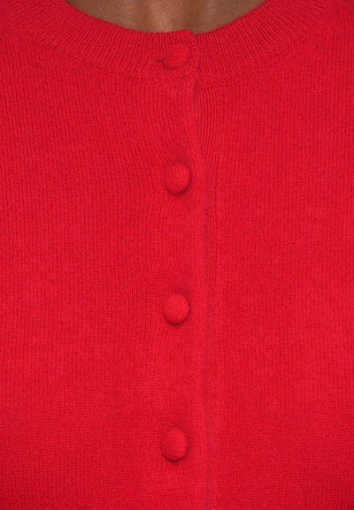 Cardigan tricotat roșu, cu guler rotund și trei nasturi asortați pe față. Textură moale, cu un design ajustat.