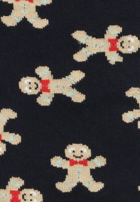 Dzianina w ciemnonawowym tle z powtarzającym się wzorem beżowych ludzików piernikowych z czerwonymi muszkami i niebieskimi akcentami lukru.