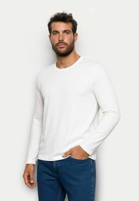 Weißes Langarmshirt mit rundem Ausschnitt, aus weichem Stoff, kombiniert mit blauen Jeans. Minimalistisches Design, keine sichtbaren Muster.
