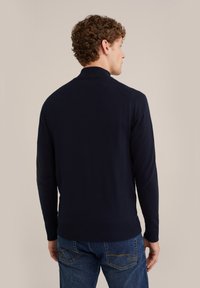 Marinblå stickad tröja med hög krage, ribbad mudd och nederkant. Baksidan har en slät yta och en figursydd design.