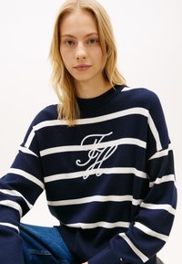 Πουλόβερ σε ναυτικό μπλε και λευκές ρίγες με στρογγυλή λαιμόκοψη, διακοσμημένο με εμφανές κεντητό λογότυπο στο στήθος και ριμπ μανσέτες.