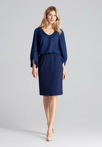 Granatowa bluzka z subtelnym blaskiem i dekoltem w kształcie litery V, zestawiona z dopasowaną granatową spódnicą. Gładka tekstura, do kolan. Beżowe szpilki.