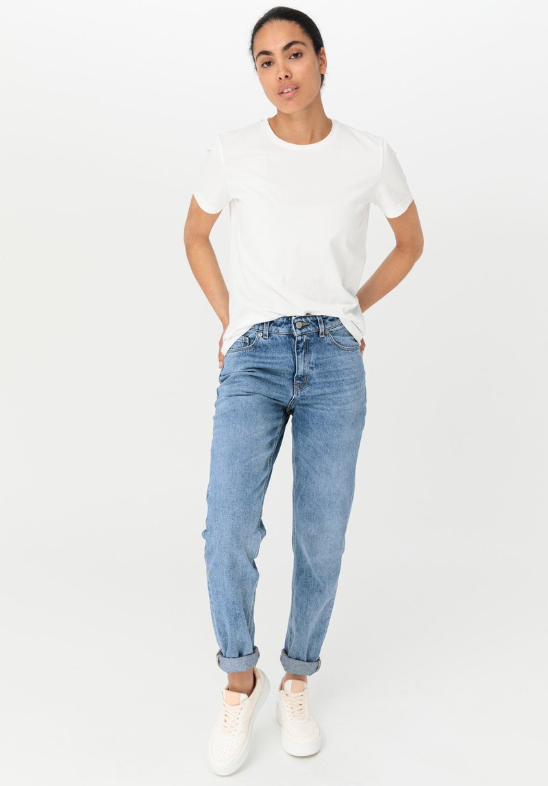 Vit T-shirt med rund hals i kombination med ljusblå jeans. Jeansen har uppvikta fållar, och modellen bär vita sneakers. Enkel, avslappnad outfit.