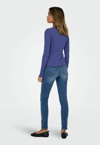 Långärmad lila ribbad topp kombinerad med blå smala jeans. Jeansen har bakfickor, och outfiten avslutas med svarta ballerinat.