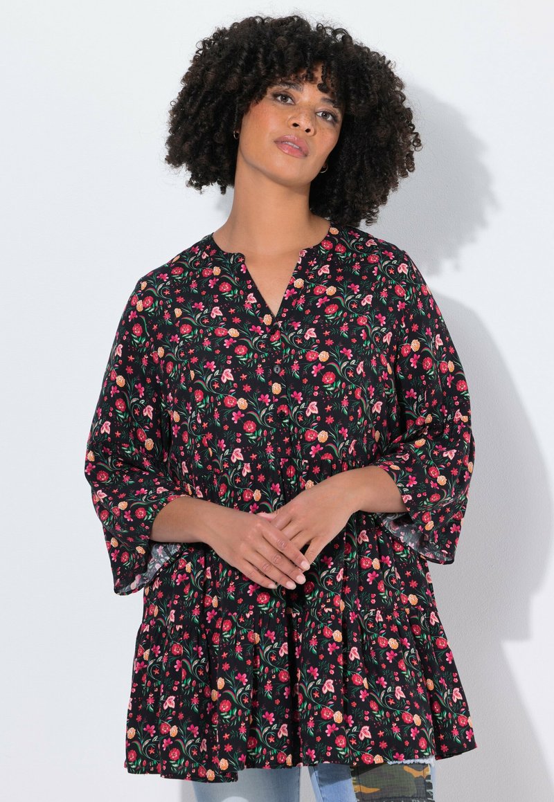 Tunique noire à motifs floraux avec un décolleté en V, des manches cloche 3/4, une taille froncée et des motifs de fleurs colorées sur un fond sombre.