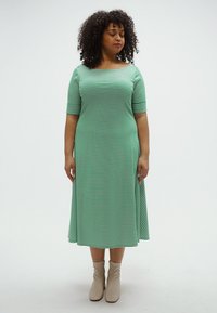 Zöld-fehér csíkos midi ruha rövid ujjakkal és egyenes szabással, világos bézs bokacsizmával párosítva. Sima pamut anyag.