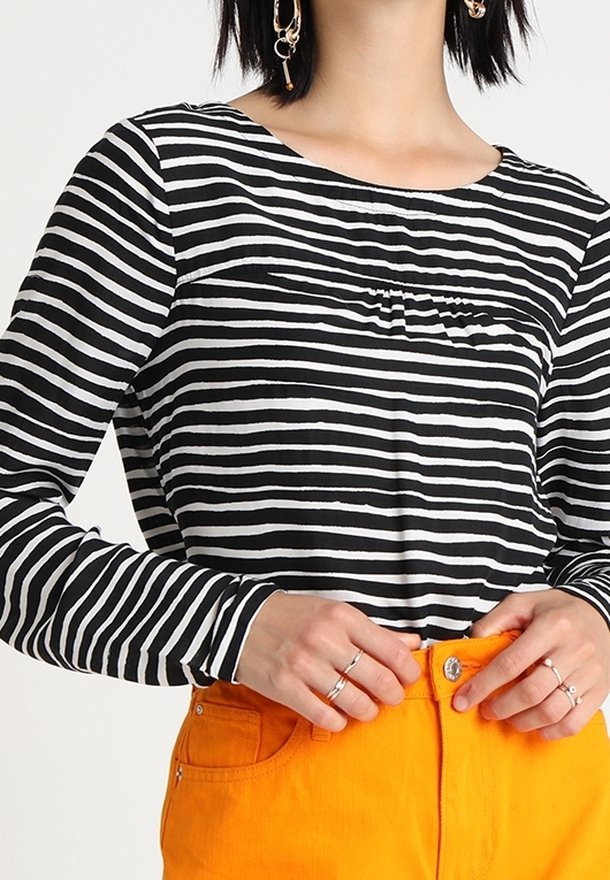 Černobílý pruhovaný top s dlouhým rukávem a kulatým výstřihem, s jemným nabíráním na prsou, kombinovaný s živě oranžovými kalhotami.