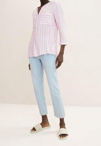 Camicia a righe rosa chiaro e bianca con due tasche sul petto, abbinata a jeans blu chiaro a vita alta e sandali beige.