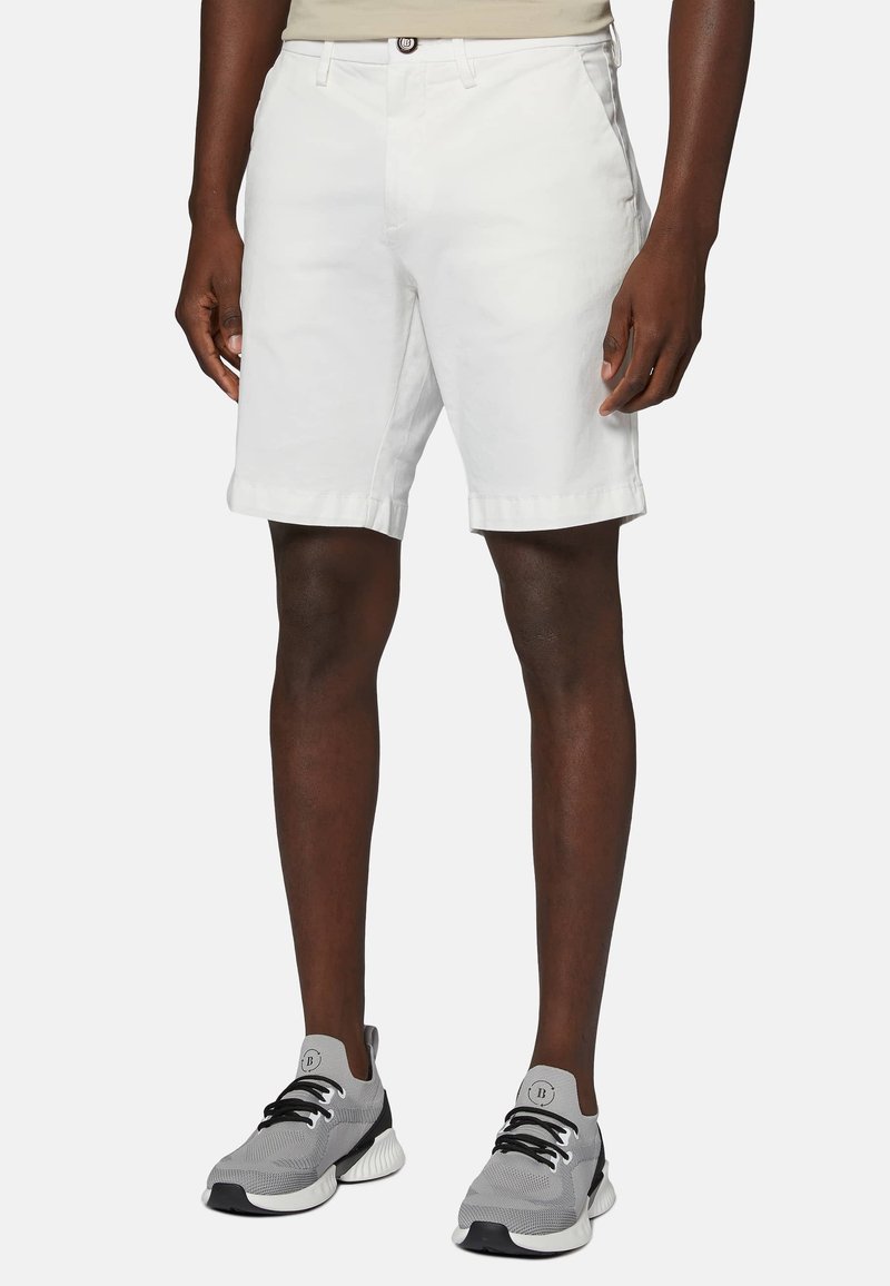 Vita bomullsshorts med regular fit, rullad nederkant, framfickor och en brun knappstängning, ihopparat med gråa sportskor.