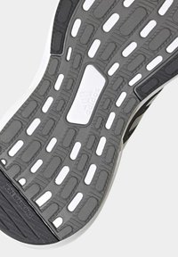 La suela del zapato presenta un diseño de goma texturizada gris con acentos blancos. Incluye recortes para flexibilidad y un panel blanco con la marca. Superficie que no deja marcas.