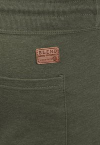 Olive zielone spodnie dresowe o miękkiej fakturze, z prążkowanym pasa i brązową skórzaną metką, na której widnieje napis "BLEND GLOBAL JEANSHIRTS."