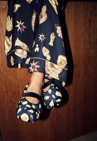 Scarpe décolleté blu scuro con motivo testurizzato di fiori e conchiglie, con punta arrotondata e cinturini in velluto nero. Pantaloni fluente con motivo visibili sopra.