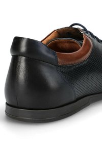 Czarne skórzane buty z perforowanym wzorem i brązowym skórzanym akcentem przy kołnierzu. Posiadają zaokrąglony obcas i gumową podeszwę.