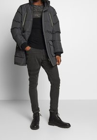 Ciemnoszara ocieplana kurtka z neonowozielonymi zamkami błyskawicznymi, czarny dzianinowy sweter, ciemnoszare dżinsy oraz czarne sznurowane botki z wytrzymałymi podeszwami.