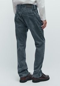 Mørkegrå denimjeans med straight-leg skæring. Har to baglommer og et lædermærke på taljen. Sammen med brune sko.
