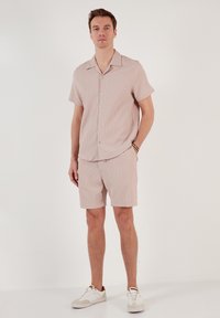 Korte mouwen, roze gestreept shirt met een kraag, gecombineerd met bijpassende shorts, gemaakt van lichtgewicht stof. Witte sneakers maken de outfit compleet.