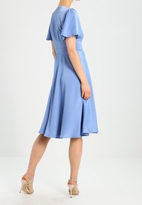 Lichtblauwe jurk met korte flapmouwen, getailleerd lijfje en een A-lijn rok die tot halverwege de kuit valt, met een soepele textuur.