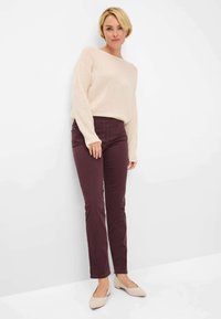 Bordeaux farvede bomuldsbukser med slim fit og frontlommer, kombineret med en blød beige strikket sweater. Flade beige sko fuldender outfittet.