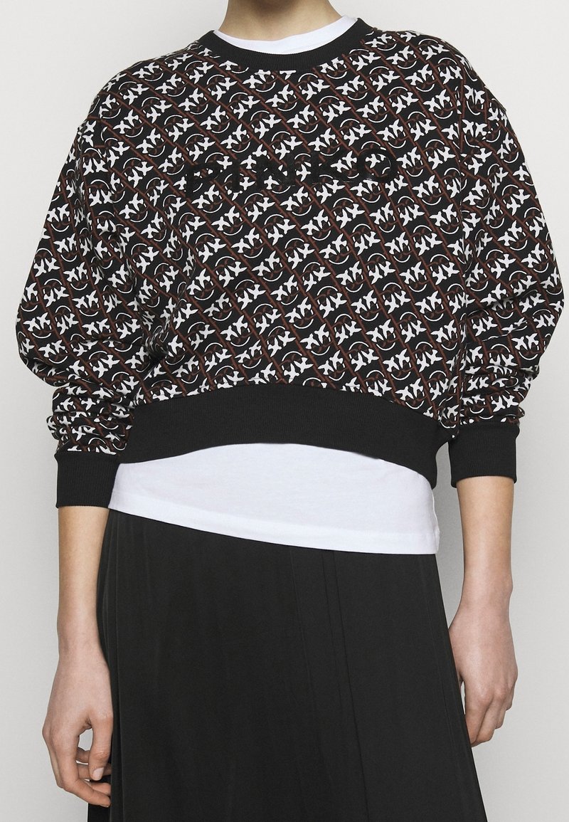 Czarna i biała bluza z wzorem, z prążkowanym okrągłym dekoltem i elastycznymi mankietami, noszona na białej koszuli, zestawiona z czarną spódnicą.