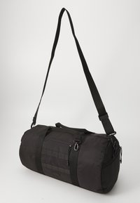 Sac de sport noir en tissu durable, avec une forme arrondie, une bandoulière ajustable et des poches zippées pour le rangement.