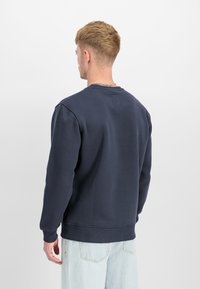 Jūras zila crewneck svīteris ar ribotām aprocēm un apakšu, izgatavots no mīksta auduma. Aizmugurē ir mazs auduma ievilkums.